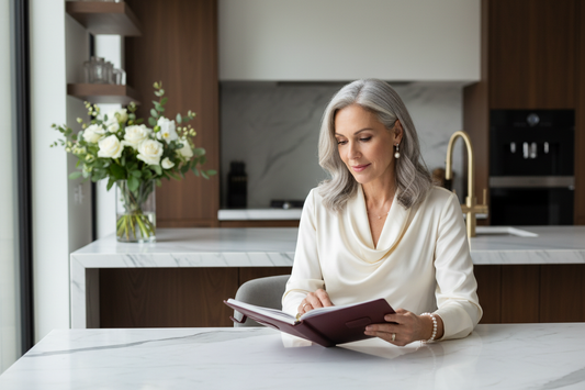Elegant woman in a luxurious home setting calmly reviewing her wellness planner with fresh flowers and soft natural light