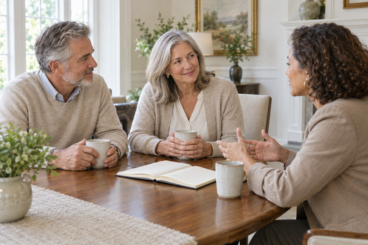 Three adults talking around a table with notebooks and mugs in a bright home.