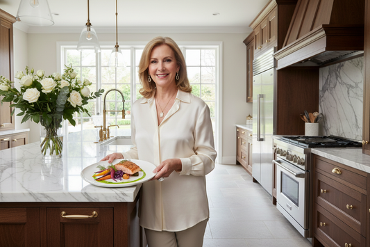 Elegant woman in her 50s in a stunning luxury kitchen holding a beautifully plated colorful meal, radiant and content, soft natural light and fresh flowers